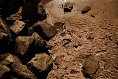 Dalgalı ve taşlı kumun dokulu arka planı. Kahverengi arkaplan, kum dokusu ve kayalar, dalgalı desen.