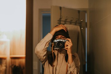 Banyodaki aynaya yansıyan fotoğraf makineli bir kızın portresi.