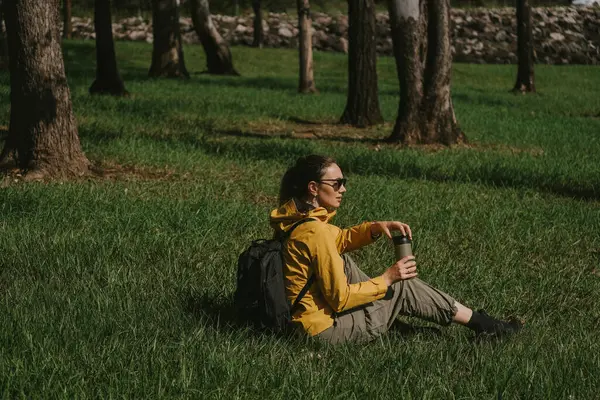 Sarı yağmurluklu, siyah sırt çantalı yeşil taklavatlı bir kadın.