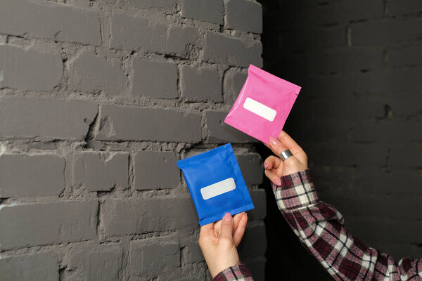 Человек, держащий две маленькие сумки в синем и розовом цветах с белыми ярлыками с серой кирпичной стеной на заднем плане. Изображения макетов для рекламных или товарных витрин и создания проектов. Макет продукта. Концепция дизайна.