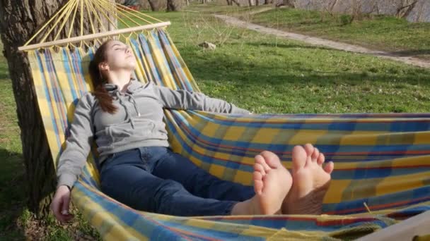 素足でハンモックの上に寝そべっている美しい女の子 — ストック動画