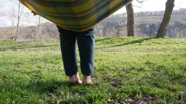 少女は草の上のハンモックから起き上がった 日当たりの良い草の上に美しい女性の足 — ストック動画