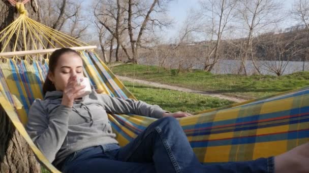 少女は自然の中でハンモックに横たわってお茶を飲む — ストック動画