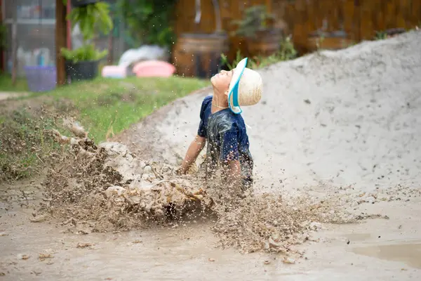 Child enjoys playing in mud pit and sand, embracing nature\'s playground in all seasons