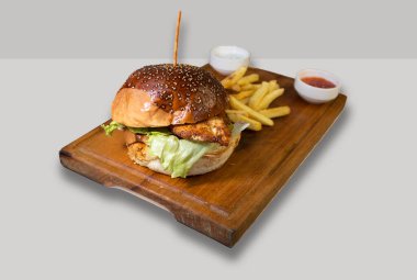 Kızarmış tavuk burger, patates kızartması ve sosla birlikte beyaz arka planda izole edilmiş.