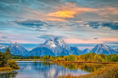 A tree-lined Oxbow Bend with Mount Moran in the background under a cloudy sky in Grand Teton National Park