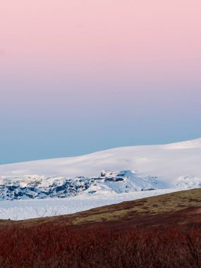 Güney İzlanda 'da güneş doğarken kar tepelerinin üzerinde pembe bir gökyüzü.