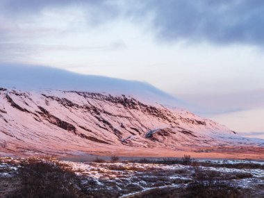 İzlanda 'nın merkezinde karla kaplı bir dağın kenarındaki pembe gün doğumu parıltısı.