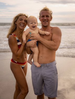 Mutlu aile kumsalda vakit geçiriyor. Baba ve anne kucağında bebek var. Anne, baba ve oğul gülümsüyor. Olumlu duygular. Asya 'da yaz tatili. Aile plajı konsepti. Seminyak plajı, Bali