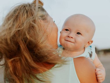 Sarı saçlı beyaz bir annenin portresi ve oğlu kumsalda vakit geçiriyor. Anne kucağında bebek var. Yaz tatili. Aile kavramı. Mutlu bir çocukluk. Arkadan bak. Seminyak, Bali, Endonezya