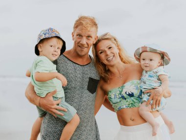 Kafkas ailesinin sahilde vakit geçirdiği portreyi yakından çek. Anne ve baba oğullarını kucaklıyor. Sevimli erkek bebekler. Gülümseyen ebeveynler. Asya 'da yaz tatili. Aile ilişkileri. Seminyak, Bali