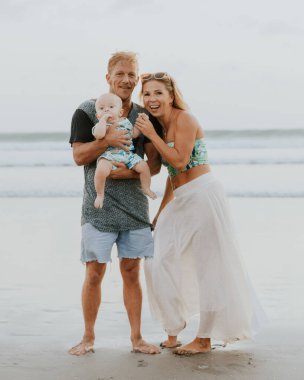 Beyaz bir aile kumsalda vakit geçiriyor. Baba kucağında bebek var. Gülümseyen anne, baba ve oğul. Mutlu bir çocukluk. Asya 'da yaz tatili. Aile ilişkileri. Seminyak Sahili, Bali, Endonezya