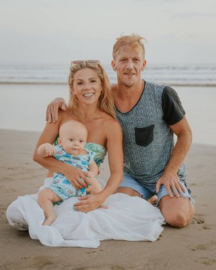 Kafkas ailesi kumsalda vakit geçirir, kumsalda otururlar. Anne kucağında bebek var. Gülümseyen anne, baba ve oğul. Mutlu bir çocukluk. Asya 'da yaz tatili. Aile ilişkileri. Seminyak, Bali