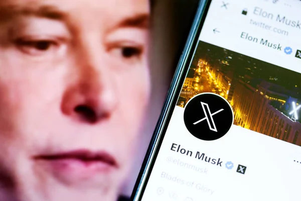 stock image Elon Musks Twitter profile on a smartphone and Elon Musk in the background.