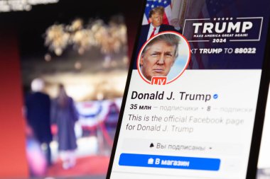 20 Ocak 2025. Ukrayna. Poltava. Akıllı telefon ekranında Donald Trump 'ın Facebook hesabı var. Arka planda Trump ve Melania Trump 'ın bir laptop ekranında odak dışı bir Facebook iletisi var..