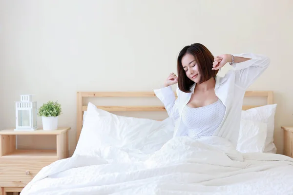 自宅でリラックスして目が覚めた後にベッドに座ってストレッチカジュアルで幸せなアジアの女性 寝室の背景を持つ美しい実業家 ライフスタイルコンセプト — ストック写真