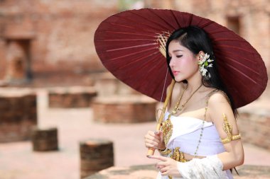 Genç moda ve güzel Asyalı kadın Tayland beyaz geleneksel kostümü ve kırmızı antika şemsiyeli antik Ayutthaya, Tayland tapınağında dikiliyor.