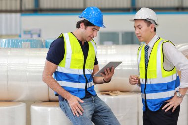 Koruyucu üniformalı bir grup mühendis ve işadamı ayakta duruyor ve tartışıyorlar, araştırıyorlar, beyin fırtınası yapıyorlar ve planlıyorlar sanayi imalat fabrikasında tabletle birlikte çalışıyorlar.