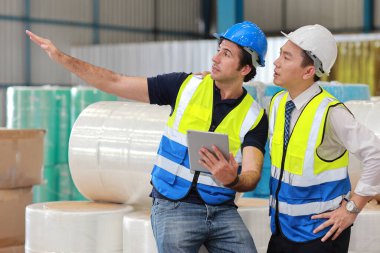 Koruyucu üniformalı bir grup mühendis ve işadamı ayakta duruyor ve tartışıyorlar, araştırıyorlar, beyin fırtınası yapıyorlar ve planlıyorlar sanayi imalat fabrikasında tabletle birlikte çalışıyorlar.