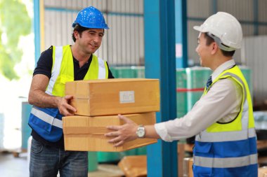 Bir grup depo çalışanı kutuları tutuyor ve büyük bir depoya paket kutusunu götürüyor veya yüklüyorlar. Depo endüstri binasındaki işleri kontrol eden Kafkas işletme yöneticisi. 