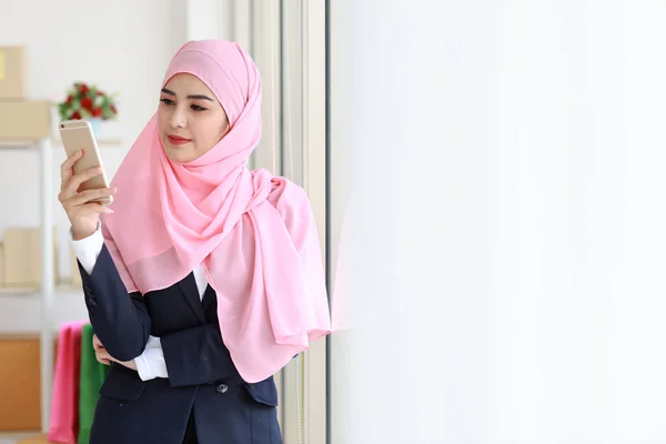 身穿蓝色西服 头戴粉色竖杆的亚洲宗教穆斯林妇女站在那里 自信地使用手机 商务妇女站在包装中小企业箱交付背景 家庭工作概念 — 图库照片