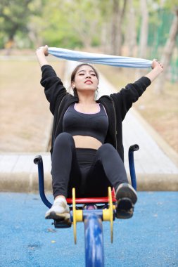 Mutlu gülümseyen, güzel Asyalı kadın spor giyim mağazasında egzersiz makinesinde dinleniyor. Şirin ve sportif kız bisikletle çalışıyor ve açık havada cep telefonu kullanıyor.