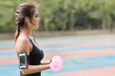 Spor giyimli, genç ve güzel bir Asyalı kadın sabah egzersizi için dambılları kaldırıyor. Aktif kız, ağaç köklü pazı egzersizi yapıyor. Spor konsepti