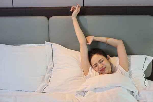 Happy young asian woman in white lingerie lying in bed, wake up late and overslept morning while doing stretching. Cute girl look comfortable, need more sleep. Difficult morning get up concept