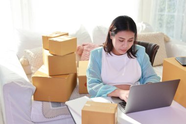 Çekici mutlu Asyalı hamile kadın oturuyor, cep telefonu kullanıyor ve tabletli müşterileri kontrol ediyor. Müstakbel anne hamilelik konsepti sırasında bebek doğurmaya hazırlanıyor ve çalışıyor..