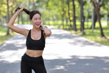 Mutlu Asyalı genç sporcu kadın portresi. Yoga esneme ve meditasyon egzersizleri. Sabah koşusu bittikten sonra açık havada. Güzel sporcu gülümseyen kadın parkta ağacın altında müzik dinliyor.