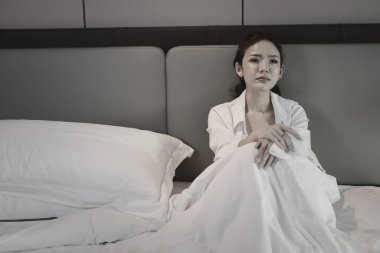 Depresyonda olan Asyalı genç bir kadın, düşük aydınlık çevresi olan bir otel odasında yatağında ağlarken elleri ve başıyla oturuyor. Üzgün kız, mutsuz ve yalnızlık konsepti.