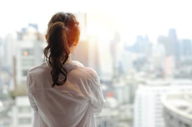 Kendine güvenen ve güzel Asyalı genç iş kadınının portresi mutlu gülümseyen yüzü ile modern bir otelde dikiliyor ve uzaklara bakıyor şehir arka planı bulanık. Başarı işi ve yaşam tarzı konsepti