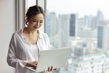 Kendine güvenen ve güzel Asyalı genç iş kadınının portresi. Mutlu duyguları olan ve modern otellerde bilgisayarını kullanan şehir geçmişi bulanık. Başarı işi ve yaşam tarzı konsepti