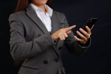 Siyah arka plan reklamları için akıllı cep telefonunda ayakta duran ve dokunan çekici profesyonel kadın elleri izole edilmiş.