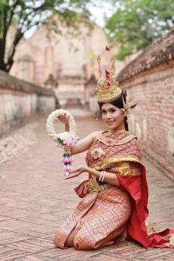 Genç moda ve güzel Asyalı kadın Tayland kırmızı geleneksel kostümü giyip elinde mutlu ve barış dolu çelenk tutarak Tayland 'daki Ayutthaya antik tapınağında dikiliyor. Seyahat kavramı