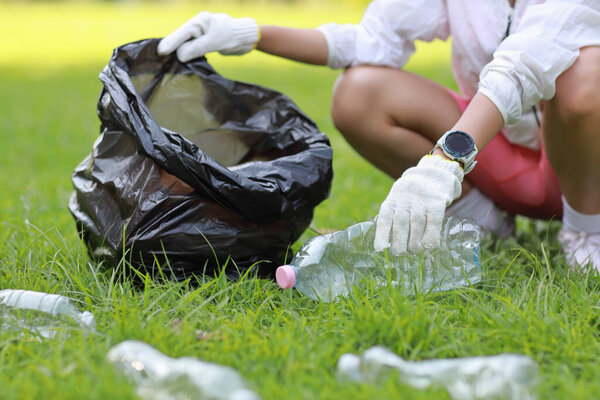 Young beautiful asian volunteer woman hands holding garbage bag and picking up litter while cleaning plastic bottle from lawn during a volunteering environmental cleanup area park event outdoors
