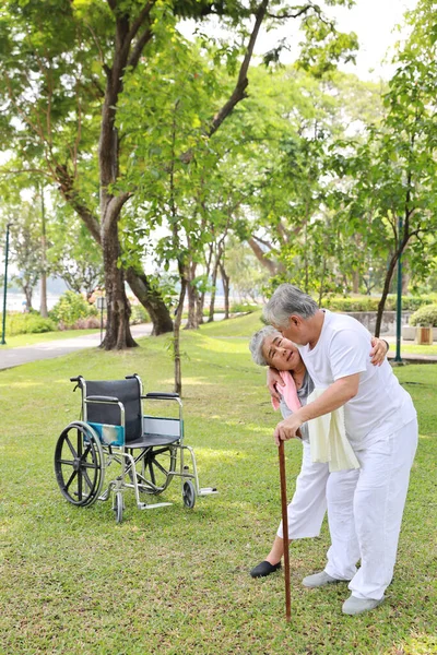 アジアのシニア女性介護者は 駐車場の屋外で車椅子と木製の棒で歩く上級男性を助け 慰めます 高齢の妻 良いヘルプケアとサポート 高齢夫の患者屋外 — ストック写真