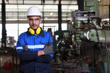 Koruyucu giysili mühendis kameraya bakarken ve kontrol ederken ve tamir ederken ağır sanayi imalat fabrikasındaki metal torna makinesinde çalışırken çapraz durdu.