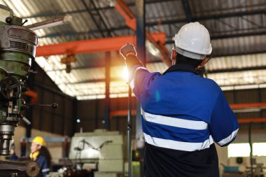 Arka görüş teknisyeni koruyucu giysi mühendisi ayakta ve telsiz kullanarak ağır sanayi imalat fabrikasında metal torna işletim makinesini kontrol ediyor veya onarıyor.