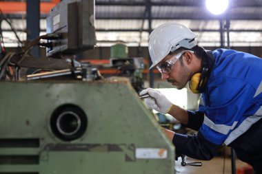 Güvenlik kaskı bakım operasyonu yapan ya da ağır sanayi imalat fabrikasındaki torna makinesini kontrol eden koruyucu üniformalı teknisyen ya da işçi. Metal çalışma kavramı