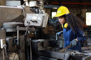 Ağır sanayi üretim fabrikasındaki torna makinesinin bakımını yaparken ya da torna yaparken elinde pano ve kamerayla koruyucu üniformalı mühendis kadın. Metal çalışma kavramı