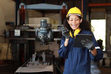 Teknisyen mühendis ya da koruyucu giysili işçi kadın ağır sanayi imalatında metal torna makinesini kontrol ederken tabletli telsiz kullanıyor.