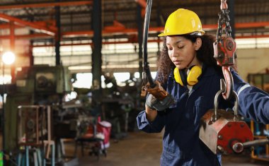 Güvenlik başlığı takmış, güvenlik önlemi almış, güvenlik önlemi almış teknisyeni ya da işçi üniformalı kadın ya da ağır sanayi imalat fabrikasında vinç uzaktan kumandasını kontrol eden.