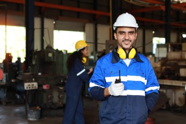 Koruyucu giysi standındaki teknisyen telsiz telsiz ve tablet kullanırken ağır sanayi imalat fabrikasındaki torna makinesini kontrol ya da bakım için çalıştırıyor.