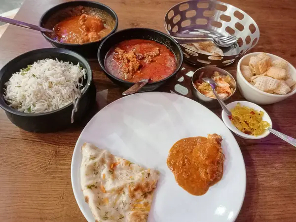 İçinde tereyağı, jeera pilavı, dum aloo, tavuk köri, koyun eti kosha, turşu ve kızarmış papad bulunan bir Doğu Hindistan restoranı yemek masası resmi..