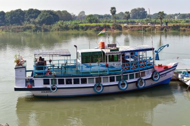 Lalbag, Batı Bengal, Hindistan 19 Ocak 2025. Görüntü, Ganj Nehri üzerindeki yeşil alanlarla çevrili geleneksel bir nehir teknesini gösteriyor. Beyaz ve mavi teknenin örtülü bir güvertesi ve Hindistan 'daki büyüleyici nehir taşımacılığını gösteren bir Kızılderili bayrağı var..
