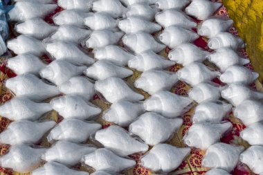 Bu resimde güzelce oyulmuş beyaz deniz kabukları güzelce plastiğe sarılmış. Yerel dilde onlara Shankha deniyor. Geleneksel işçilik ve kültürel çekiciliği vurguluyor..