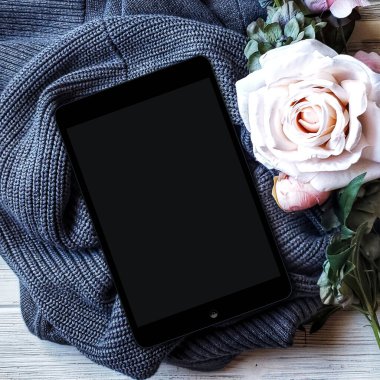 Beyaz arkaplanda boş ekranlı ipad. Kopyalama alanı olan üst görünüm. Pembe gül ve örgü süveter.