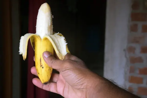 Muz kabuğu soyulmuş muzu koyu tuğladan bir arka plana yakın tut..