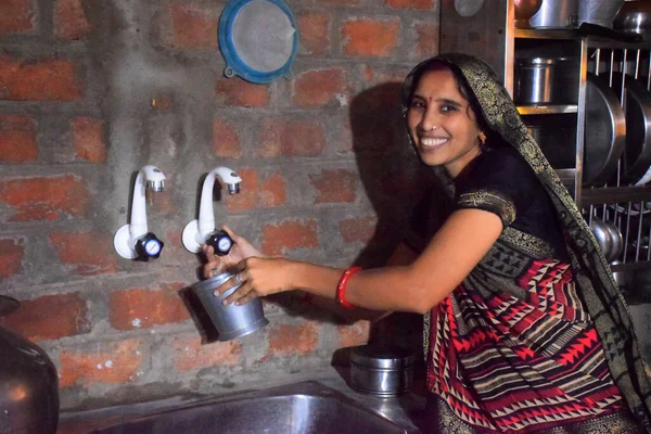 Indian rural housewife washes utensils in the kitchen with tap water. brick wall background